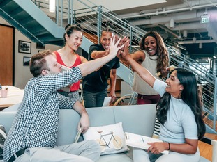 Diverse group of adult students sharing a group high-five in a modern campus lounge, celebrating collaboration and returning to school.