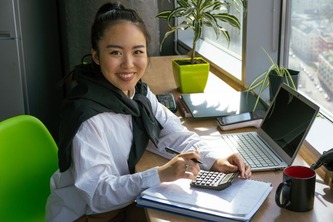 Accounting and finance student working with a calculator, notebook and laptop at a desk