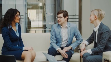 Three business professionals in a modern office discussing a project, showing the teamwork skills gained with a business management degree